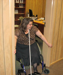 Treva finds it is often easier to maneuver through doorways, such as this one to her office at the NFB-Jernigan Institute, by tucking her cane under her chin and using her arms to pull herself through the doorframe. 