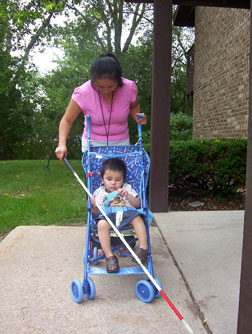 Sweeping with a long white cane as she goes, a mom pushes her child in a stroller. The child touches the cane to find out what his mother is up to. Check out Using the Teaching Cane