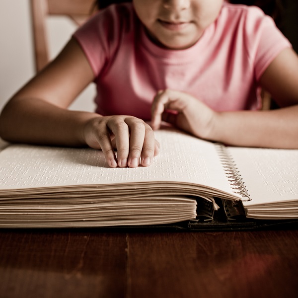 A young girl reads Braille paper.