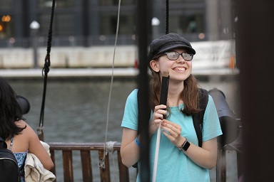 Taryn stands on a boat in the Baltimore Harbor holding her white cane.